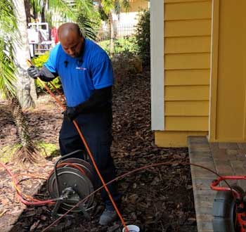 Plumber Cleaning a Drain on Side of House