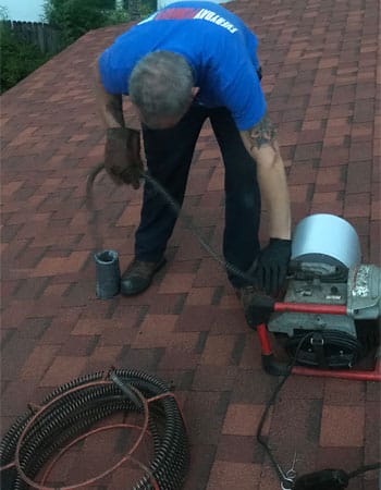Plumber on Roof Cleaning a Drain Through a Vent Stack
