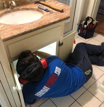 Plumber under a sink fixing a leaking pipe