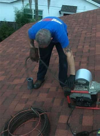 Plumber on Roof with Drain Cleaning Machine Clearing a Drain through A roof Vent Stack