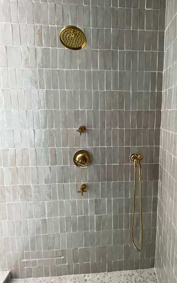 Shower Remodel - Gold Fixtures with rain head and shower handle on grey glass bathroom tile.