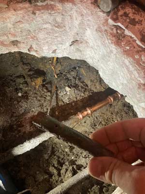 Picture of a copper pipe with a pinhole in it and the repair completed under the concrete slab.