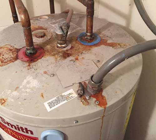 Old water heater with rusted connections and leaking