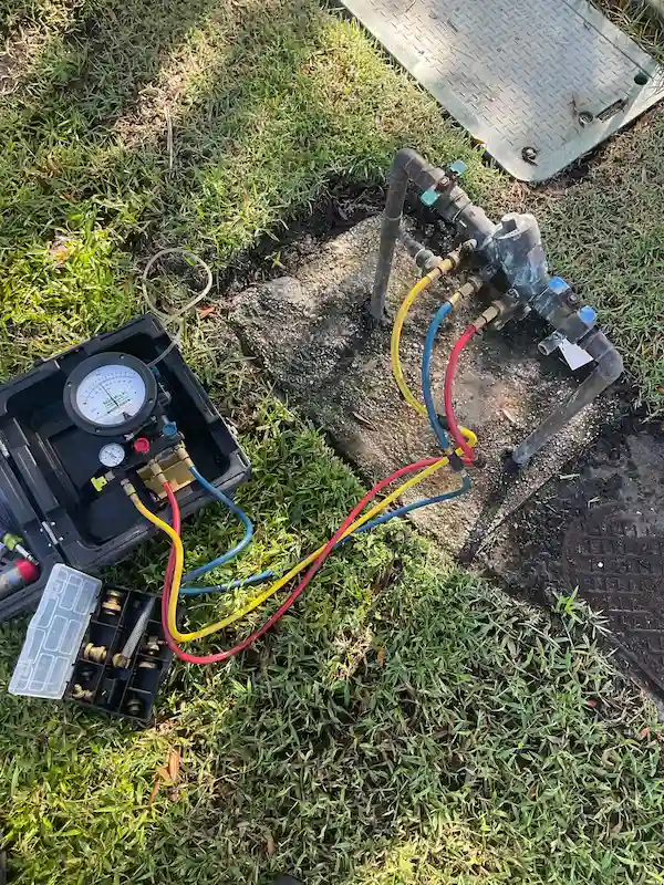 Backflow preventer device being professionally tested with pressure gauges and hoses by a Hillsborough County plumber.