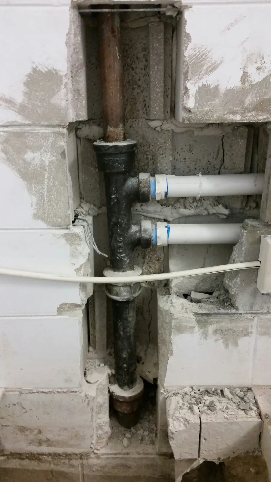 Exposed cast iron and PVC drain pipes inside a wall during a pipe repair by a Hillsborough County plumber.