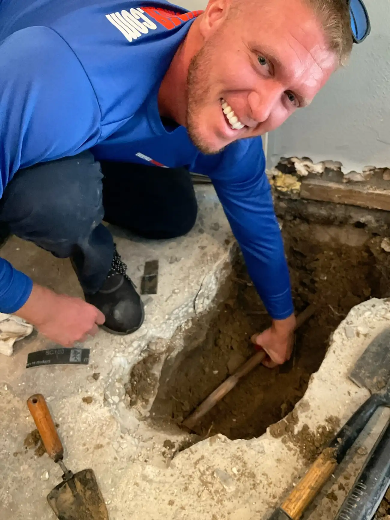 Plumber smiling while repairing underground pipe, showcasing a hands-on plumbing career opportunity in Tampa Bay.