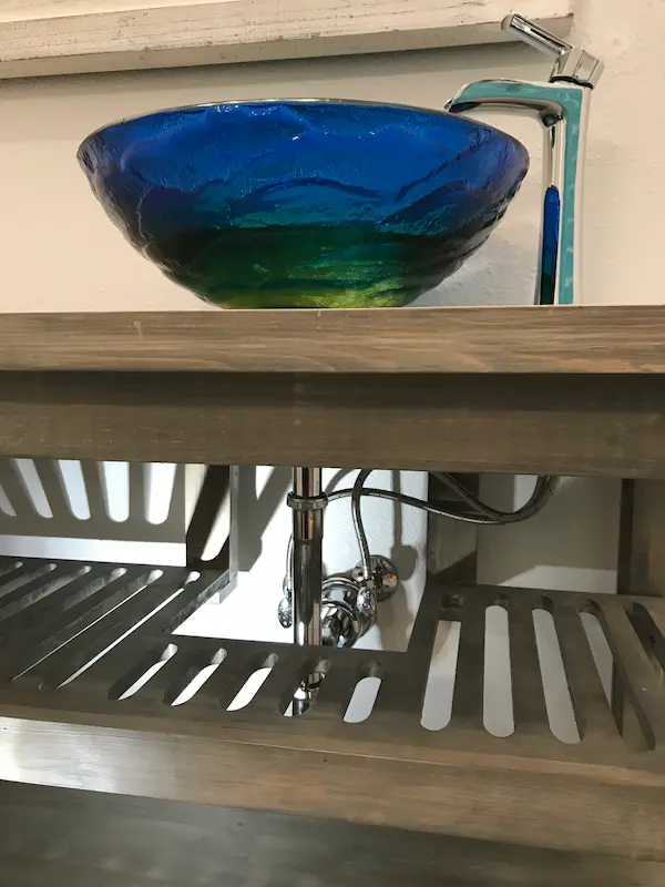 Blue glass vessel sink with modern faucet installed in a residential Tampa bathroom