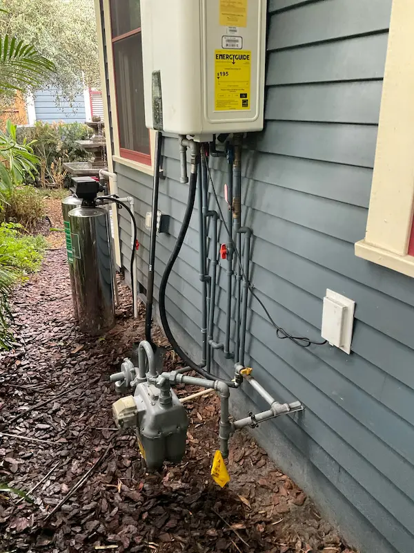 Exterior gas plumbing with meter, regulator, and black iron piping supplying a tankless water heater; shutoff valves and drip legs installed in Cheval, FL.