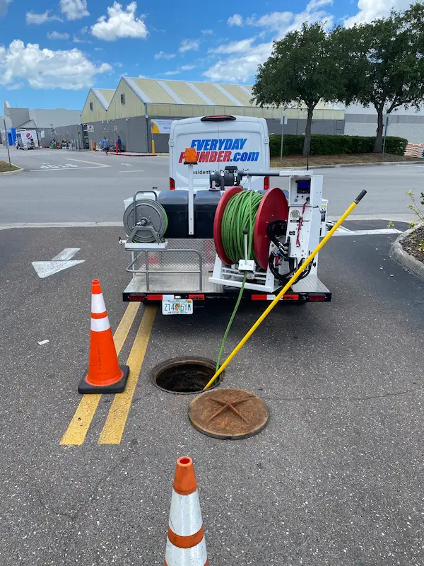 EVERYDAYPLUMBER.com service truck with hydro jetting equipment set up at an open manhole, using high-pressure hoses to clean a sewer line, with traffic cones marking the work area.