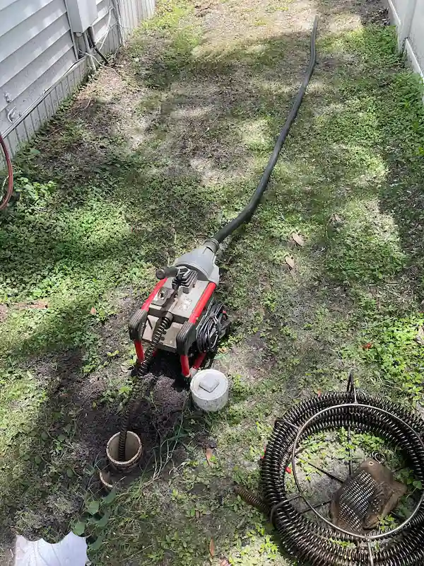 Professional drain cleaning machine snaking a sewer line through an outdoor cleanout to remove blockages and restore proper flow