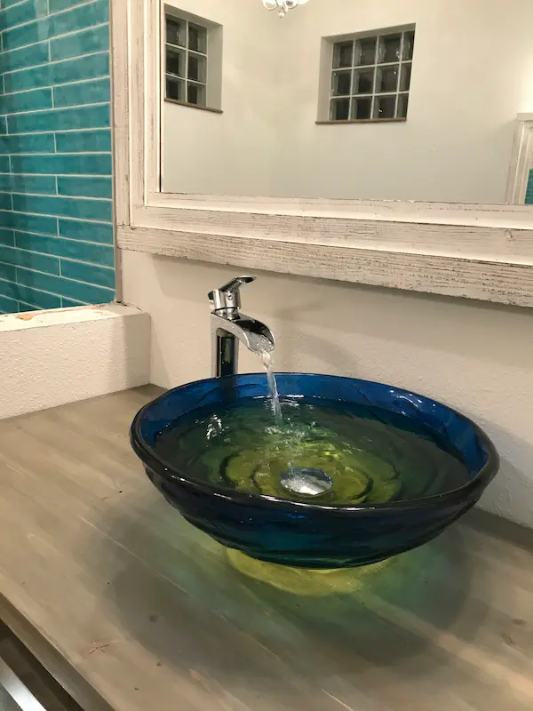 Blue glass vessel sink with single-handle faucet running, showcasing a clean residential bathroom plumbing installation.