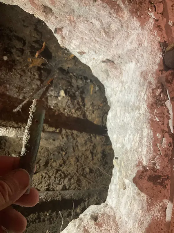 Corroded copper section removed during slab leak repair, pinhole leak exposed beneath a concrete floor opening.