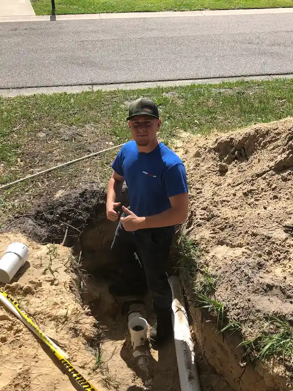 Friendly technician in trench beside PVC sewer line during repair—clean, professional service from St. Petersburg plumbers at EVERYDAYPLUMBER.com