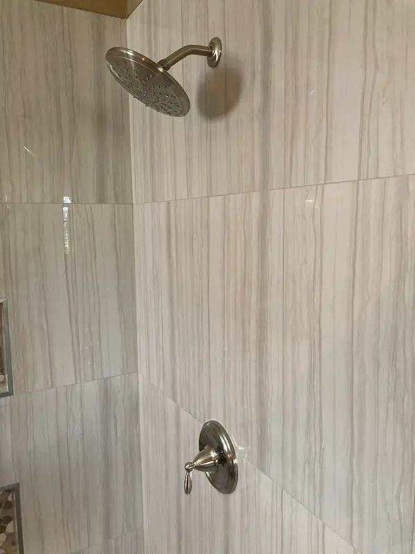Shower valve replacement with rain shower head on a tiled shower wall in Tampa, FL.