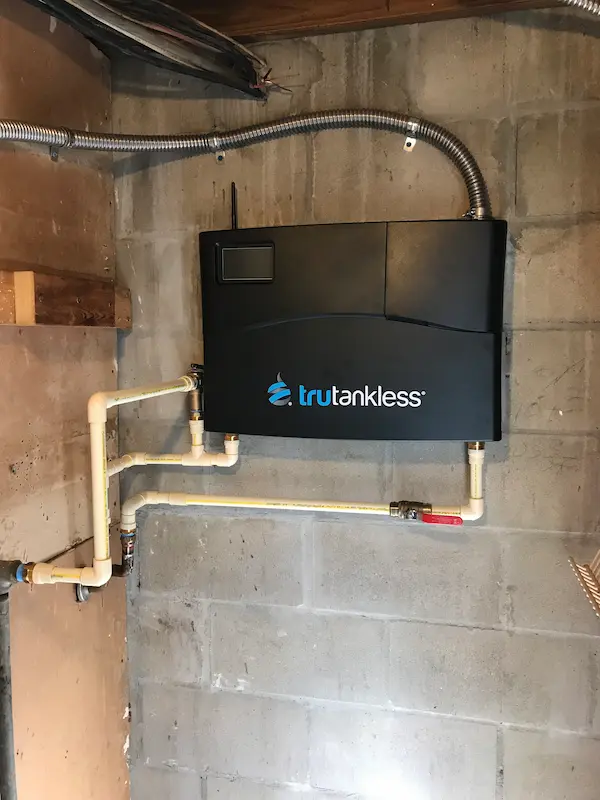 Wall-mounted electric tankless water heater by Trutankless, professionally installed with PVC piping in a concrete block utility room.
