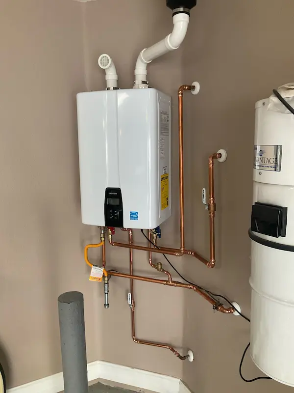 Professionally installed tankless water heater mounted on an interior wall, featuring neatly arranged copper piping, gas line, and venting for a clean, efficient setup.