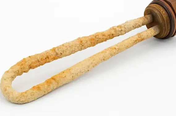 Close-up of a corroded water heater heating element covered in thick mineral scale buildup from prolonged exposure to high-mineral water.