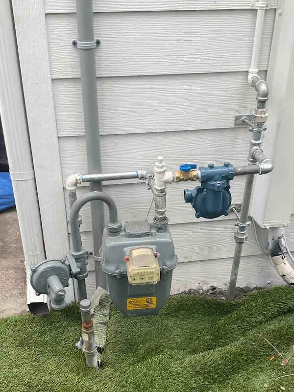 Natural gas meter with regulator, shutoff valve, and galvanized gas line plumbing on an exterior wall