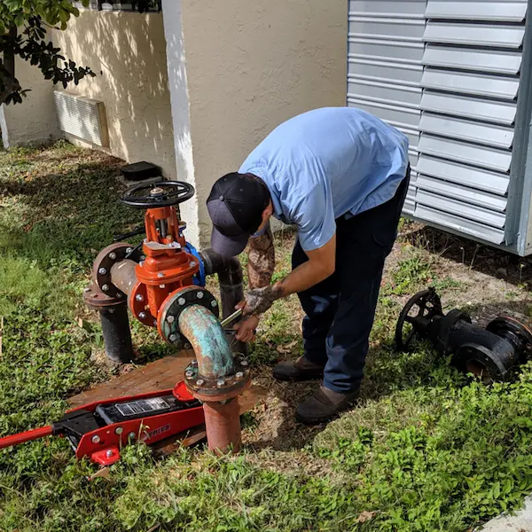 Commercial plumber repairing a backflow preventer and gate valve outside a business in Ybor City