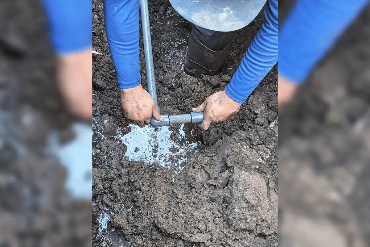 EverydayPlumber.com plumber fitting a PVC pipe connection by hand in a waterlogged excavation trench during a sewer line repair in Tampa Bay
