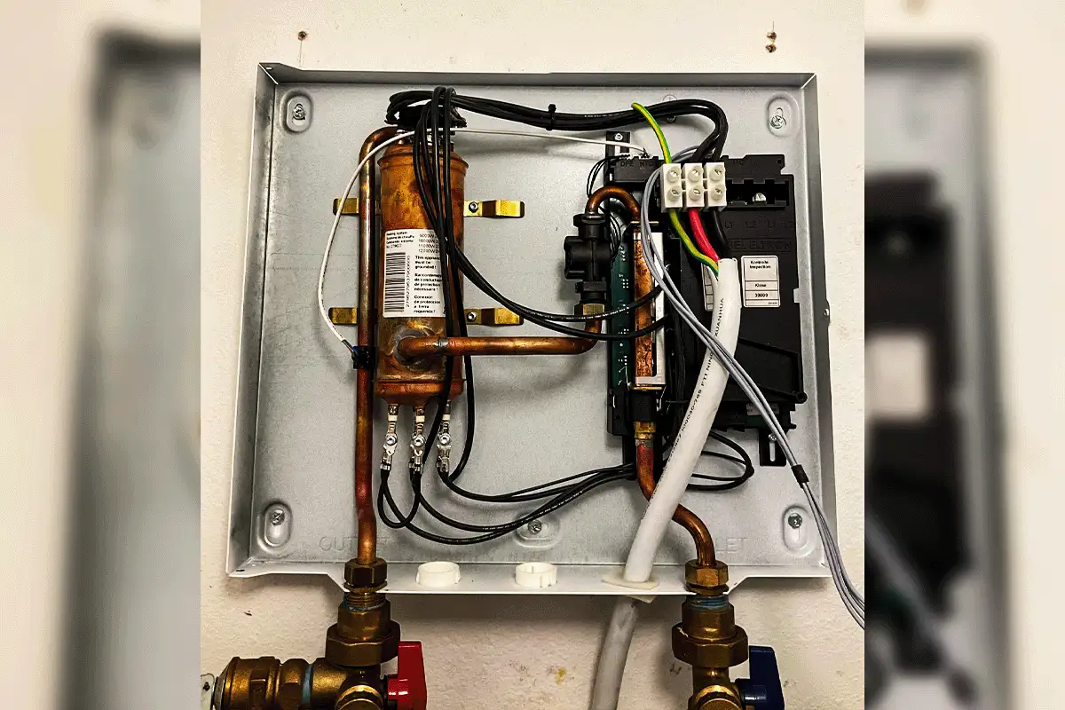 Interior of an electric tankless water heater opened during a maintenance inspection in Tampa Bay — showing copper heat exchanger coil, control board, flow sensor, and inlet and outlet brass connections that require annual descaling service in Tampa Bay's hard water conditions