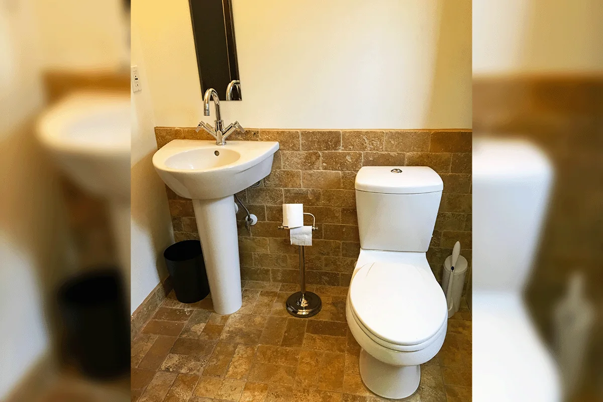 Residential bathroom with pedestal sink and toilet on travertine tile — residential plumbing Wesley Chapel — EVERYDAYPLUMBER.com Wesley Chapel