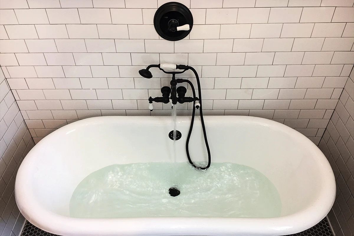 Freestanding clawfoot bathtub filling after matte black faucet and fixture installation in South Tampa home bathroom — tub and shower plumbing services in South Tampa — EVERYDAYPLUMBER.com