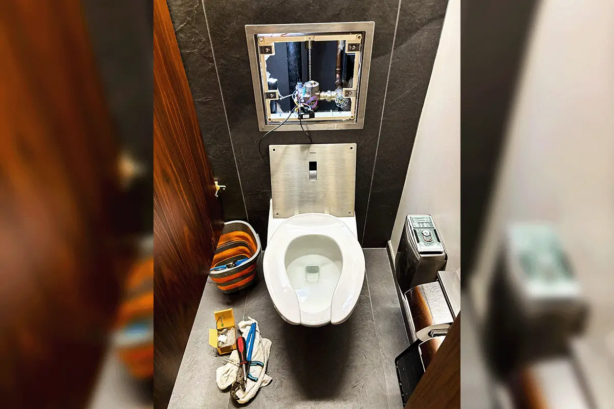 edp-toilet-repair-commercial-wall-hung-in-wall-tank-2026 Commercial wall-hung toilet with open in-wall tank access panel showing flush valve components during service — commercial toilet repair Tampa — EVERYDAYPLUMBER.com Tampa Bay