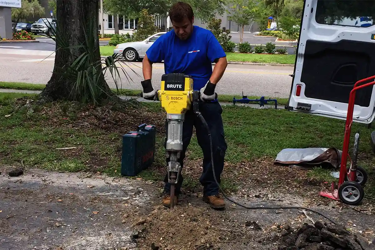 edp-concrete-jackhammer-pipe-access-2026 EVERYDAYPLUMBER.com technician breaking pavement to access an underground pipe on a commercial property — commercial plumbing repair — EVERYDAYPLUMBER.com Temple Terrace