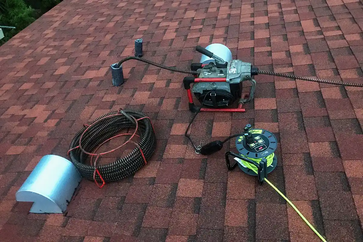 edp-drain-cable-machine-roof-vent-2026 Drain cleaning cable machine and coiled cable staged at a roof vent access point — drain cleaning service — EVERYDAYPLUMBER.com Tampa Bay