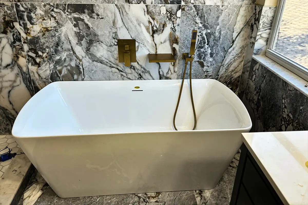 Freestanding soaking tub with brushed brass filler installed against marble bathroom walls — tub and shower valve installation — EVERYDAYPLUMBER.com Tampa Bay