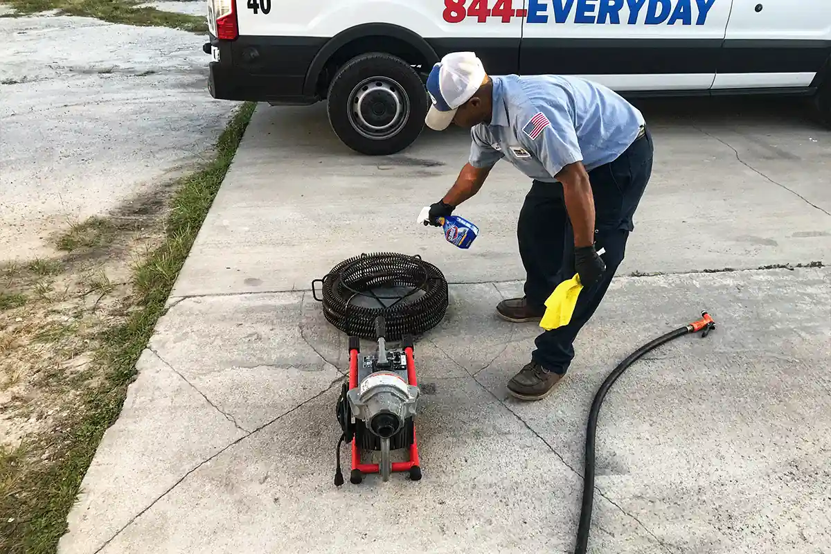 Plumber cleaning a drain cabling machine beside an EVERYDAYPLUMBER.com service van — drain and disposal service — EVERYDAYPLUMBER.com Tampa Bay